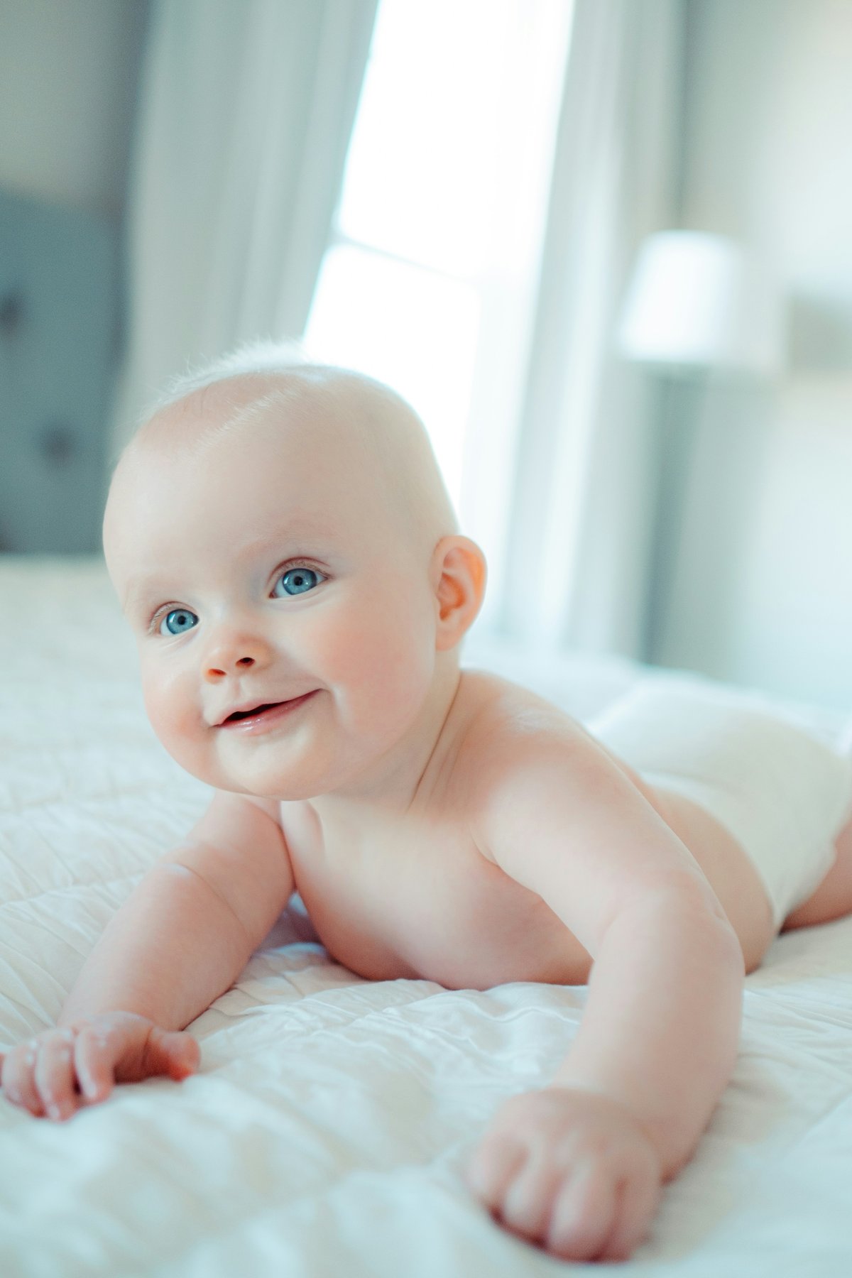 Smiling baby on white bedding in a bright, soft-lit nursery